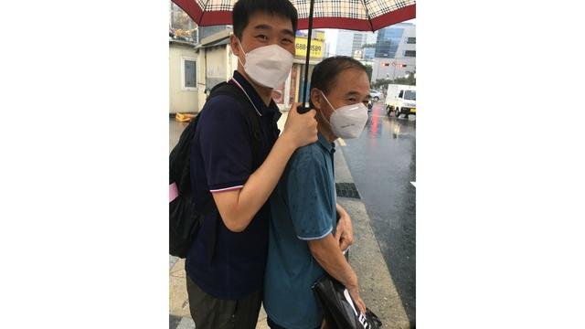 These were extremely rainy days in Korea; the author was protecting his father with an umbrella.