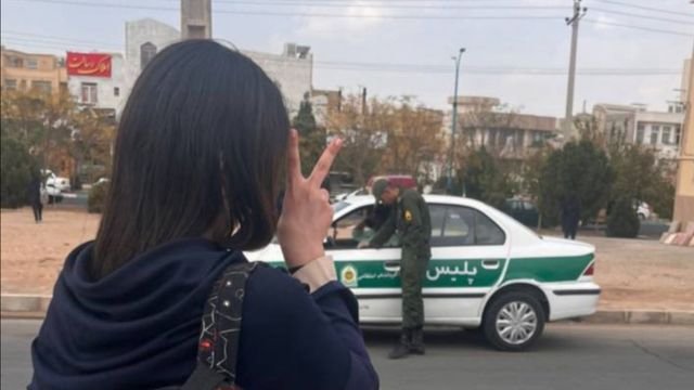 Iran, a defiant young woman makes the victory sign in front of a police car. From X.