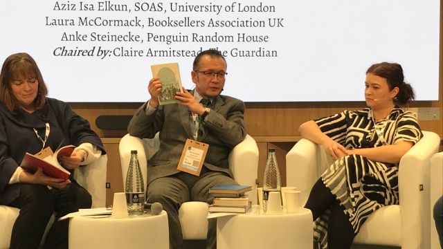 Aziz Isa Elkun lifting up one of the Uyghur poetry books banned by the Chinese state in his homeland.