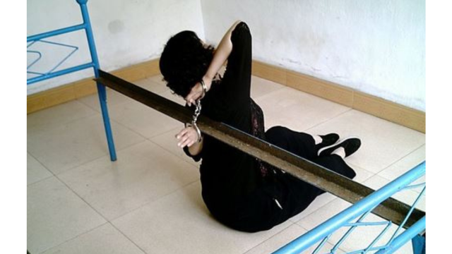 Prisoner handcuffed to a bed frame. Falun Gong reenactment.