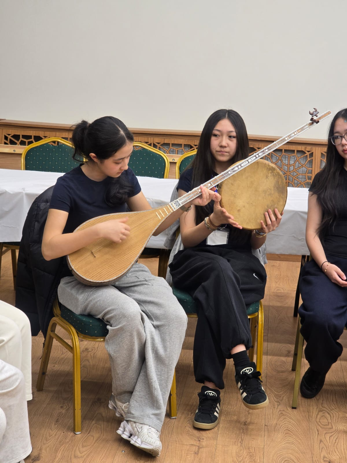 Two Uyghur girls trying out the traditional Dutar (left) and the Dap during a Uyghur music workshop at the recent cultural event for diaspora teenage youth in London. Photo by Mirkamil Turkel, used with his permission.