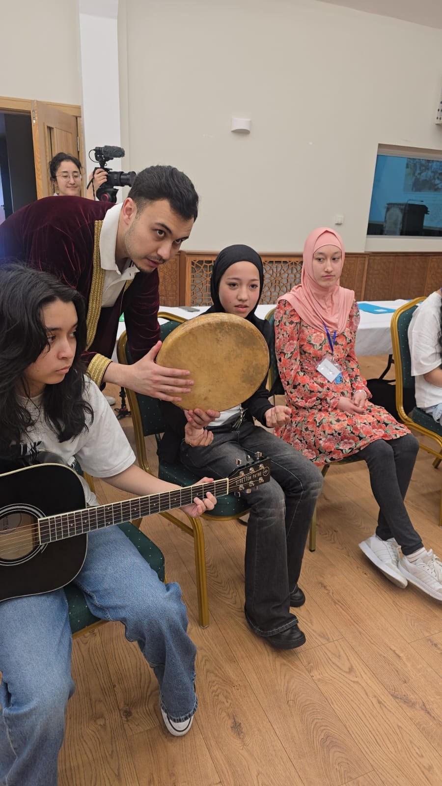 Uyghur-Norwegian musician Dilzat Turdi giving a participant in a Uyghur youth event a few tips on playing the national &ldquo;Dap&rdquo; instrument. Photo used with permission of Mirkamil Turkel.