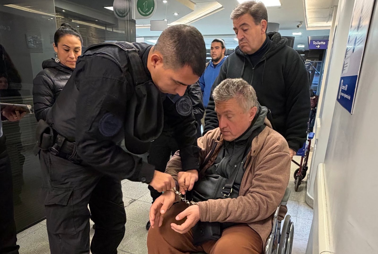 A surrealistic scene: Rudnev in his wheelchair, but with handcuffs in the hospital, as if he were at risk of escaping.